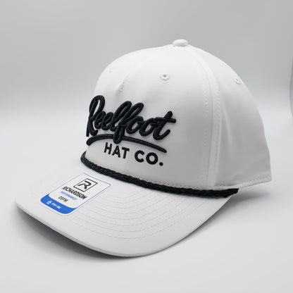 A white structured baseball cap with black embroidered 'Reelfoot HAT CO.' lettering on the front and a black elastic band under the brim, shown on a light gray studio background.