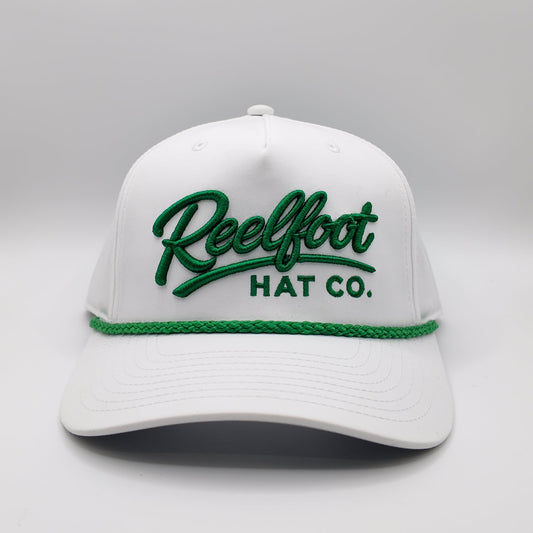 A white structured baseball cap with green embroidered 'Reelfoot HAT CO.' lettering on the front and a green braided rope detail across the brim, shown on a light gray studio background.