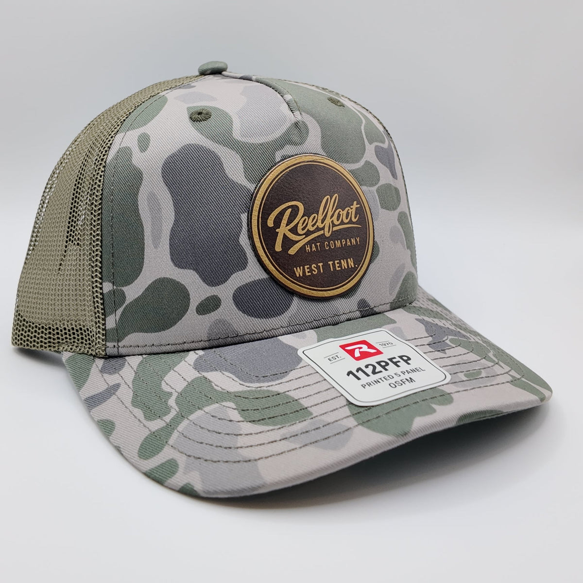 A camouflage trucker hat with a green and gray camo pattern, olive green mesh back, and a circular gold and black 'Reelfoot' patch on the front.