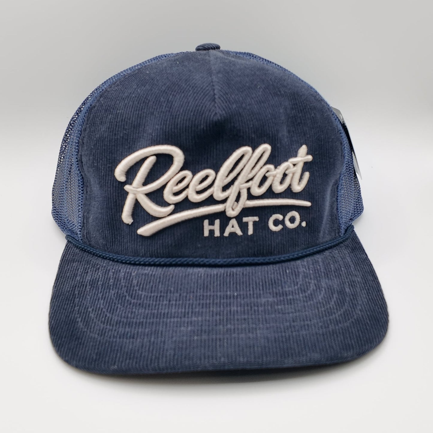 A navy blue corduroy trucker hat with white embroidered text reading 'Reelfoot HAT CO.' on the front, shown against a light gray studio background.
