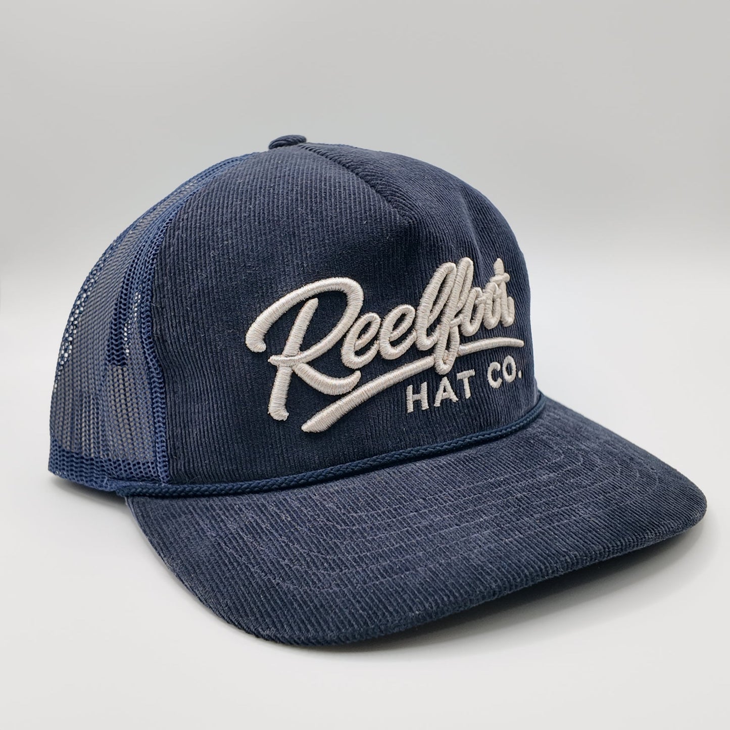 A navy blue trucker hat with a textured front panel and mesh back, featuring 'Reelfoots HAT CO.' embroidered in white script on the front.