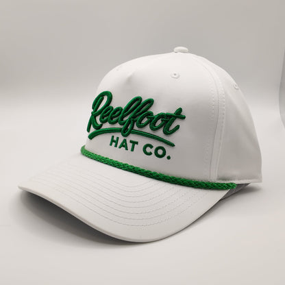 A white baseball cap with green embroidered text reading 'Reelfoot HAT CO.' on the front and a green braided trim along the brim, photographed on a light gray studio background.